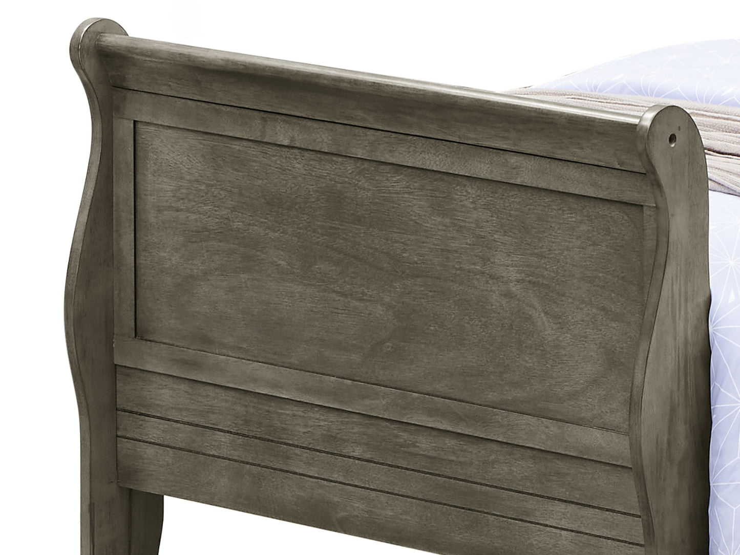 A close-up of the Panel Sleigh Bed’s wooden footboard in dark gray shows its panel design with curved top edges and visible wood grain. A portion of a mattress and blanket is seen in the background.