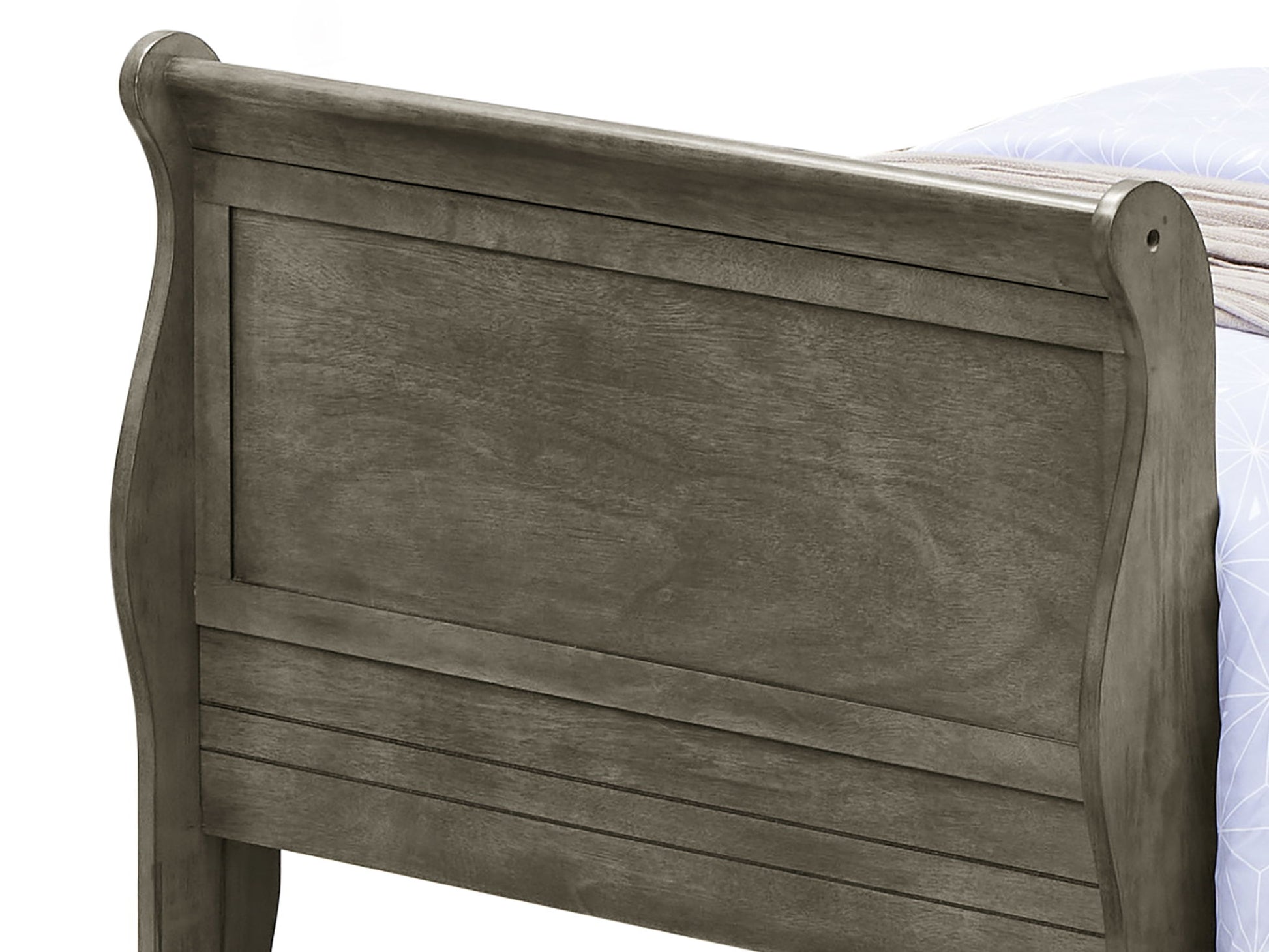 A close-up of the Panel Sleigh Bed’s wooden footboard in dark gray shows its panel design with curved top edges and visible wood grain. A portion of a mattress and blanket is seen in the background.
