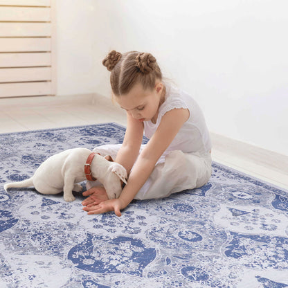 A young girl with braided hair sits on the Maval - Stunning Area Rug, gently playing with a small white puppy in a bright, minimal room with light-colored flooring.
