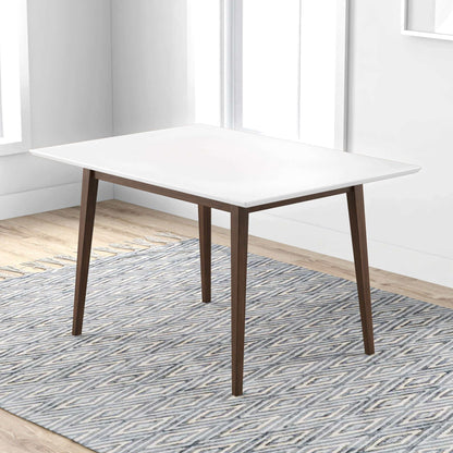 The Levi - Modern Style Rectangular Dining Kitchen Table with a white top and wooden legs stands on a patterned gray and white rug in a bright room featuring light wood floors and large windows.