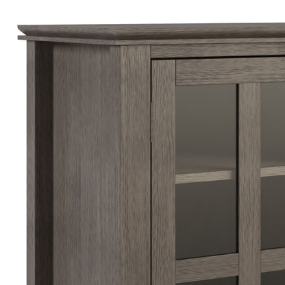 Close-up of the upper corner of the Artisan - Handcrafted, Tall TV Media Stand in a gray finish, featuring glass panel doors with interior shelves visible through the glass.