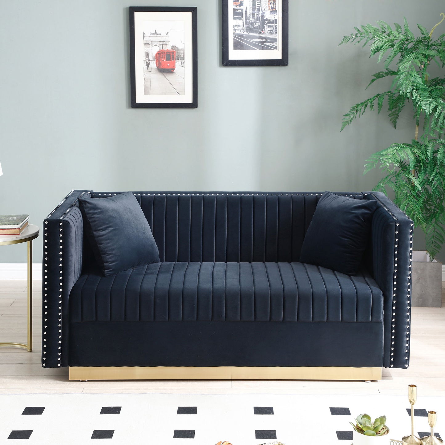 The Contemporary Vertical Channel Tufted Velvet Sofa Loveseat Upholstered 2 Pieces Set With 4 Pillows in dark blue sits by a light green wall with framed art, next to a potted plant and side table, atop a patterned rug.