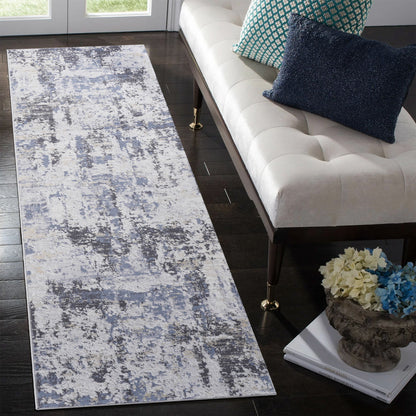 A modern hallway showcases the Payas - Abstract Area Rug in blue and gray tones on dark wood floors, paired with a white upholstered bench, blue accent pillows, and a decorative floral vase.