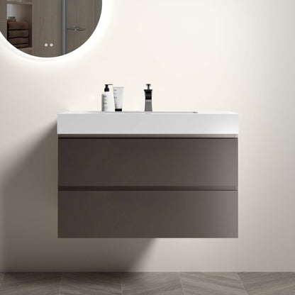 The Alice Bathroom Vanity features a white one-piece sink basin, large two-tone gray drawers, and is wall-mounted for a modern look. A round mirror hangs above, with soap dispensers on the countertop and herringbone tile flooring below.