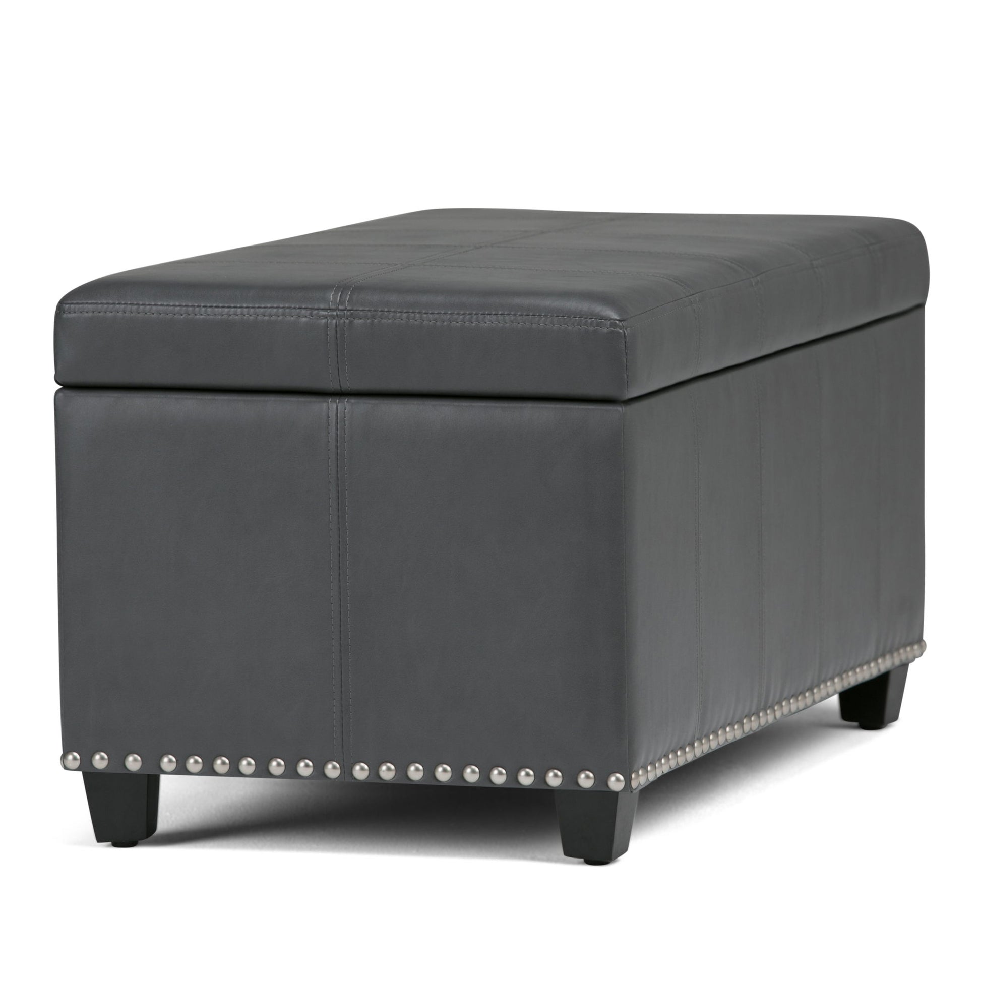 The Amelia Transitional Storage Ottoman Bench features a rectangular design in dark gray with a padded lid, decorative stitching, nailhead trim at the base, and short black legs.