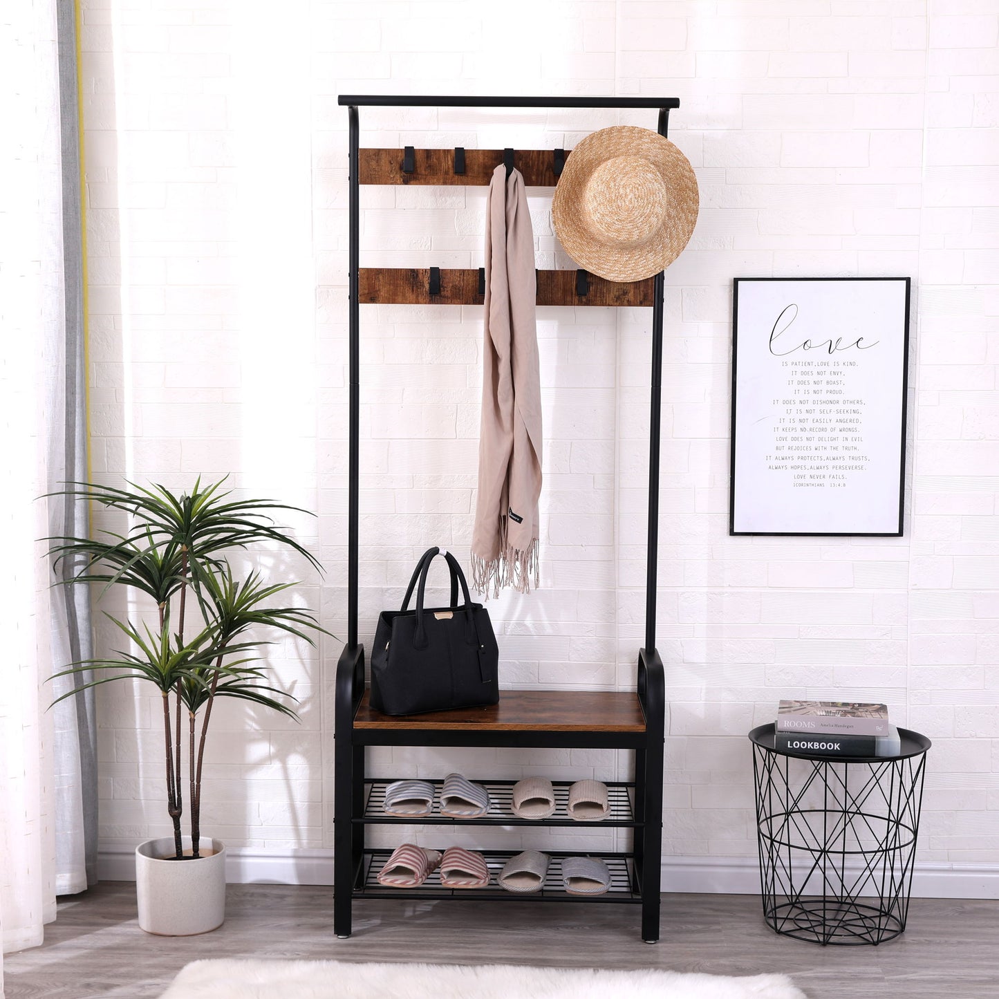 A modern entryway featuring the Hall Tree With Shoe Bench For Entryway with 9 removable hooks holding a hat and scarf, a bench with a black handbag, shoes on lower shelves, a potted plant, framed quote art, and a wire basket against a white brick wall.