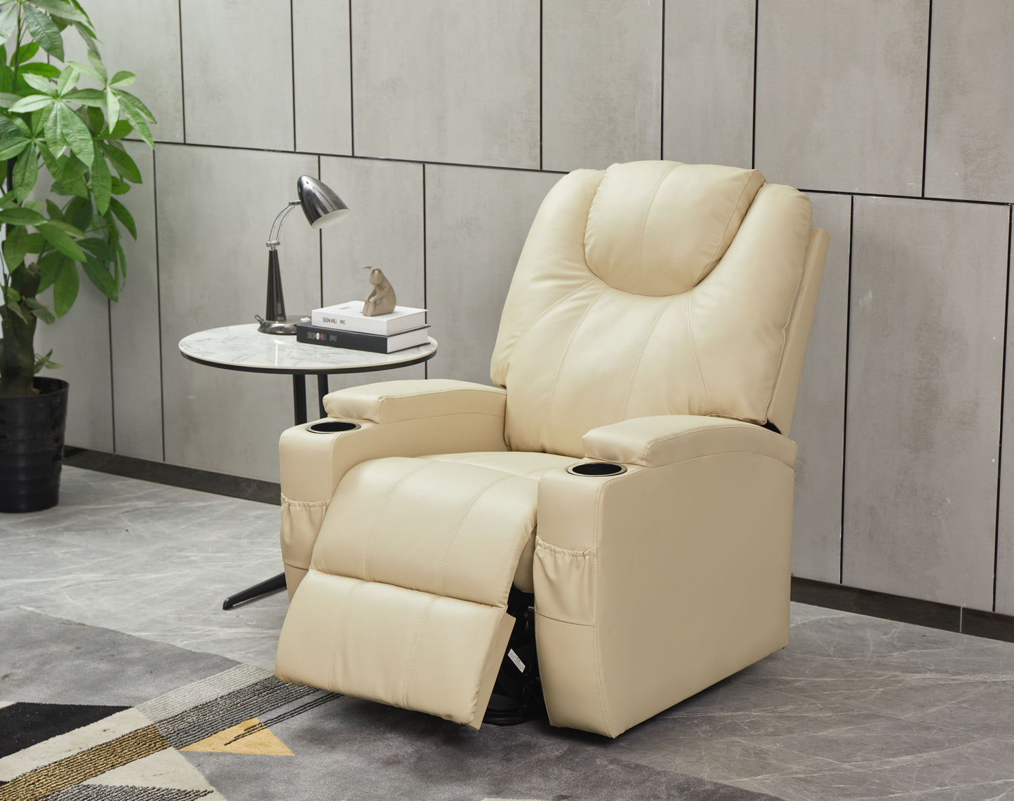 A Modern Recliner Chair With Cup Holders and Remote Control sits next to a round side table with a lamp, décor, and book. A potted plant and sleek gray wall panels are in the background.