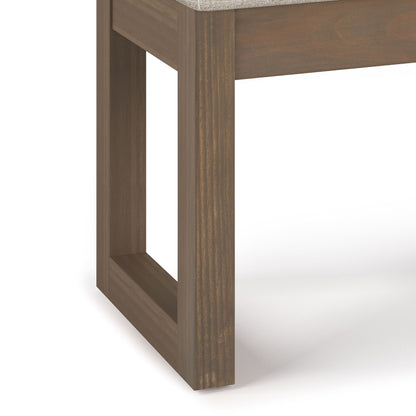 Close-up of the Milltown Upholstered Ottoman Bench featuring a rectangular, open-frame wooden leg with a smooth finish and a light-colored upholstered top, set against a white background.