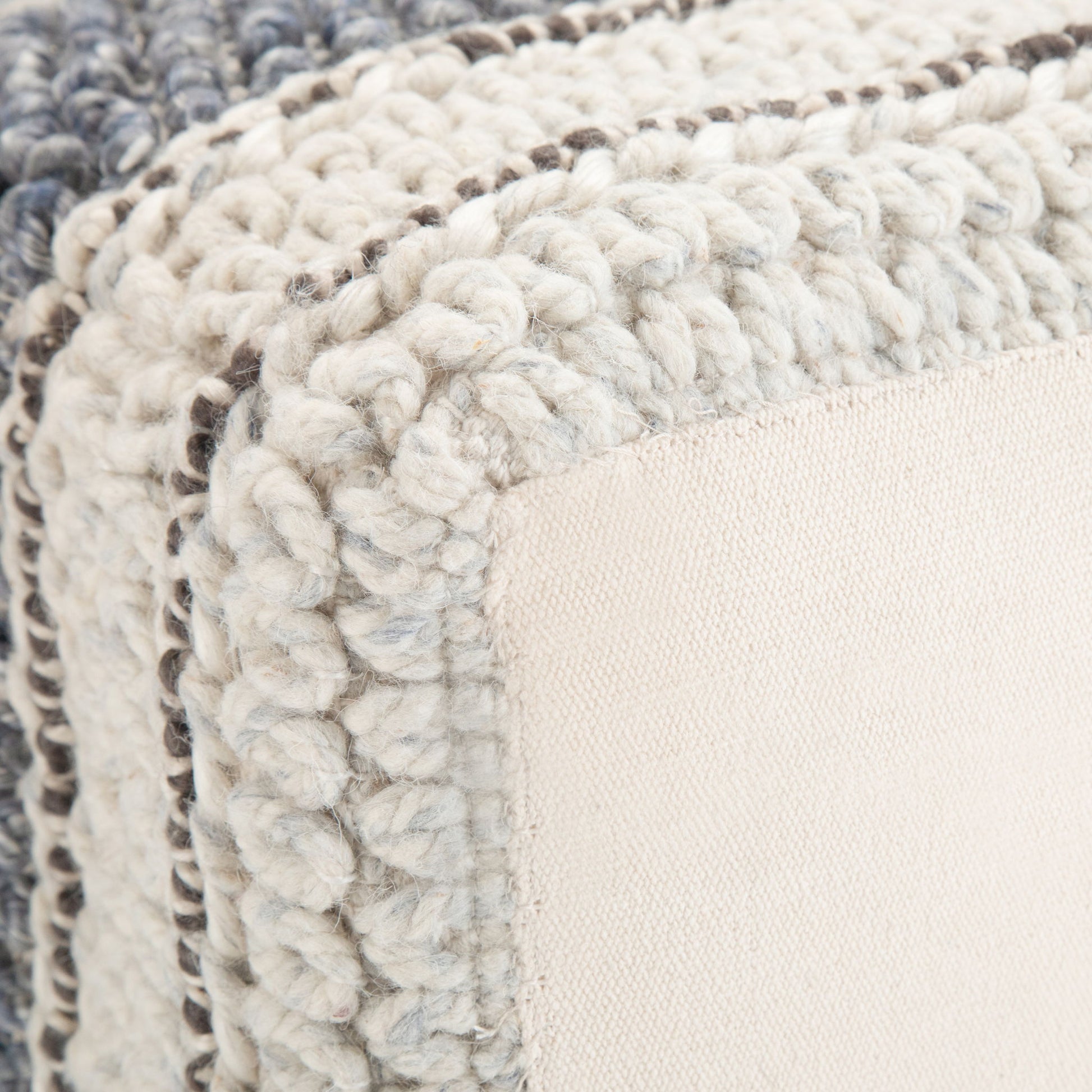 Close-up of the Grady - Handcrafted Square Pouf featuring thick, chunky knit edges in cream and gray with a smooth, light beige fabric panel at the center.