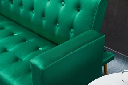 Close-up of a bright green Comfort Compact Design Sofa Bed with velvet, button-tufted upholstery and visible armrest. A white round table appears in the lower right. The background features a dark wall and gray floor.