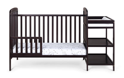 The Ramsey 3-in-1 Convertible Crib/Changer Combo is a dark wood crib with an attached changing table, two open storage shelves, and includes a white mattress with a subtle pattern.