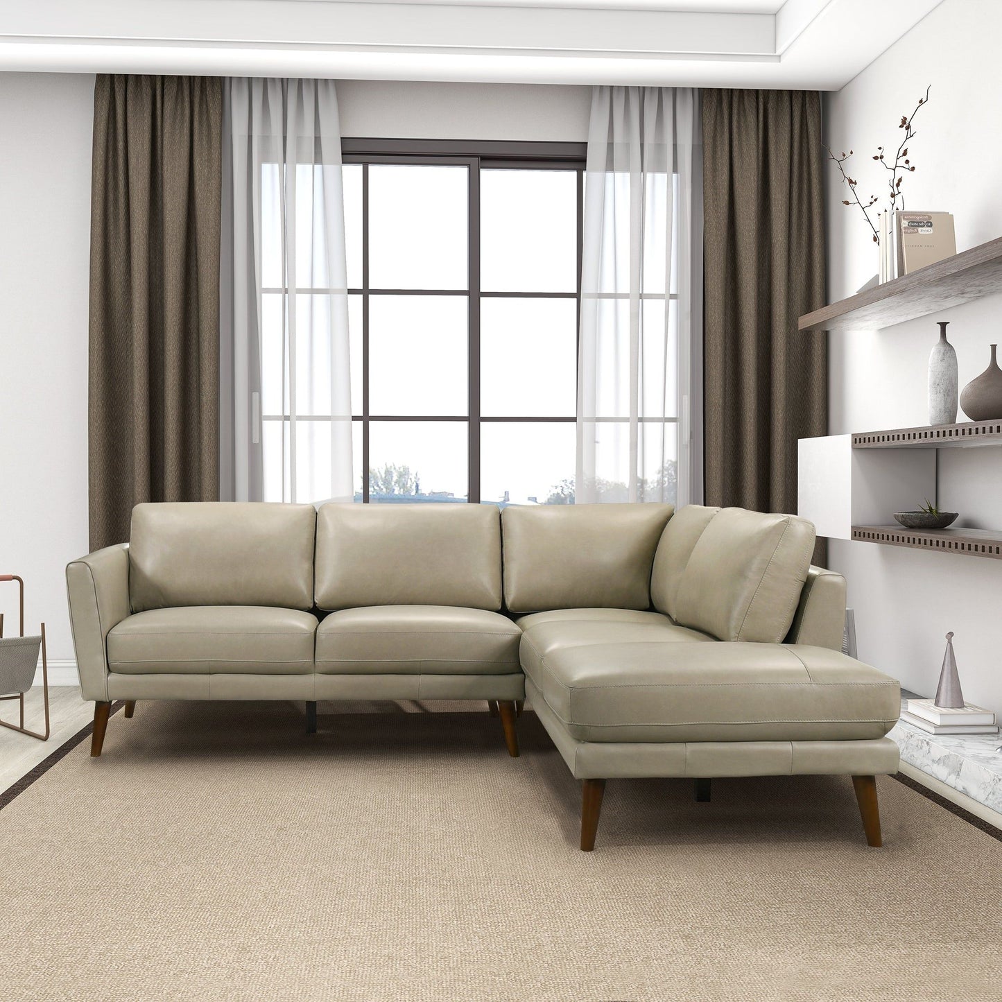A modern living room with a large window, beige curtains, and the Benson Sectional Sofa With Chaise in light gray leather on a tan rug. Shelves with decor items are mounted on the right wall.