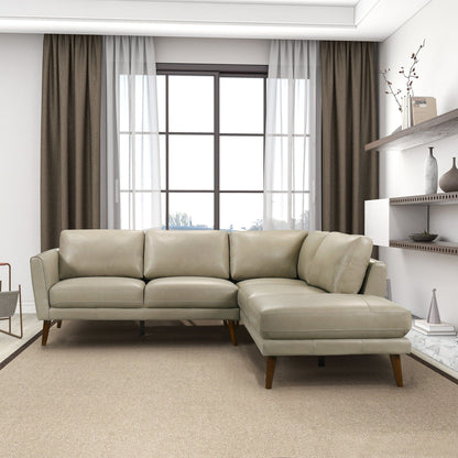 A modern living room with a large window, beige curtains, and the Benson Sectional Sofa With Chaise in light gray leather on a tan rug. Shelves with decor items are mounted on the right wall.