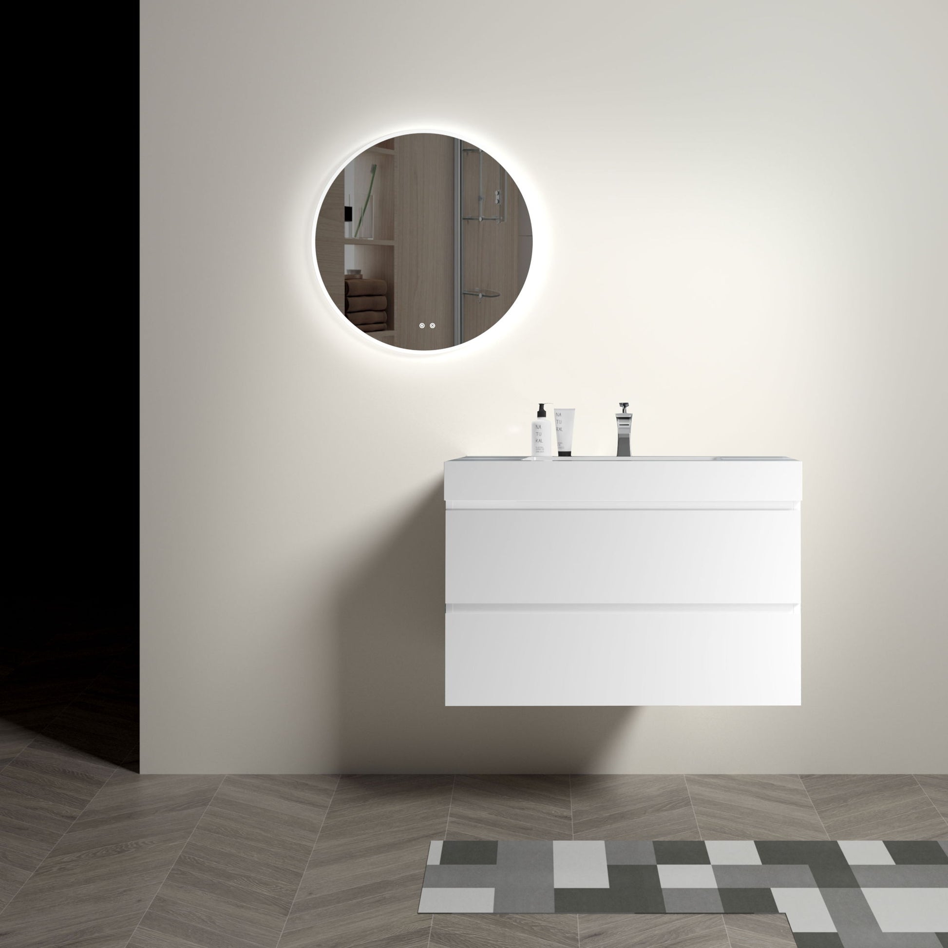 A modern minimalist bathroom features an Alice floating vanity with a one-piece sink basin below a round backlit mirror. Two soap dispensers sit atop the vanity, geometric tiles cover the floor, and the walls are painted a light neutral color.