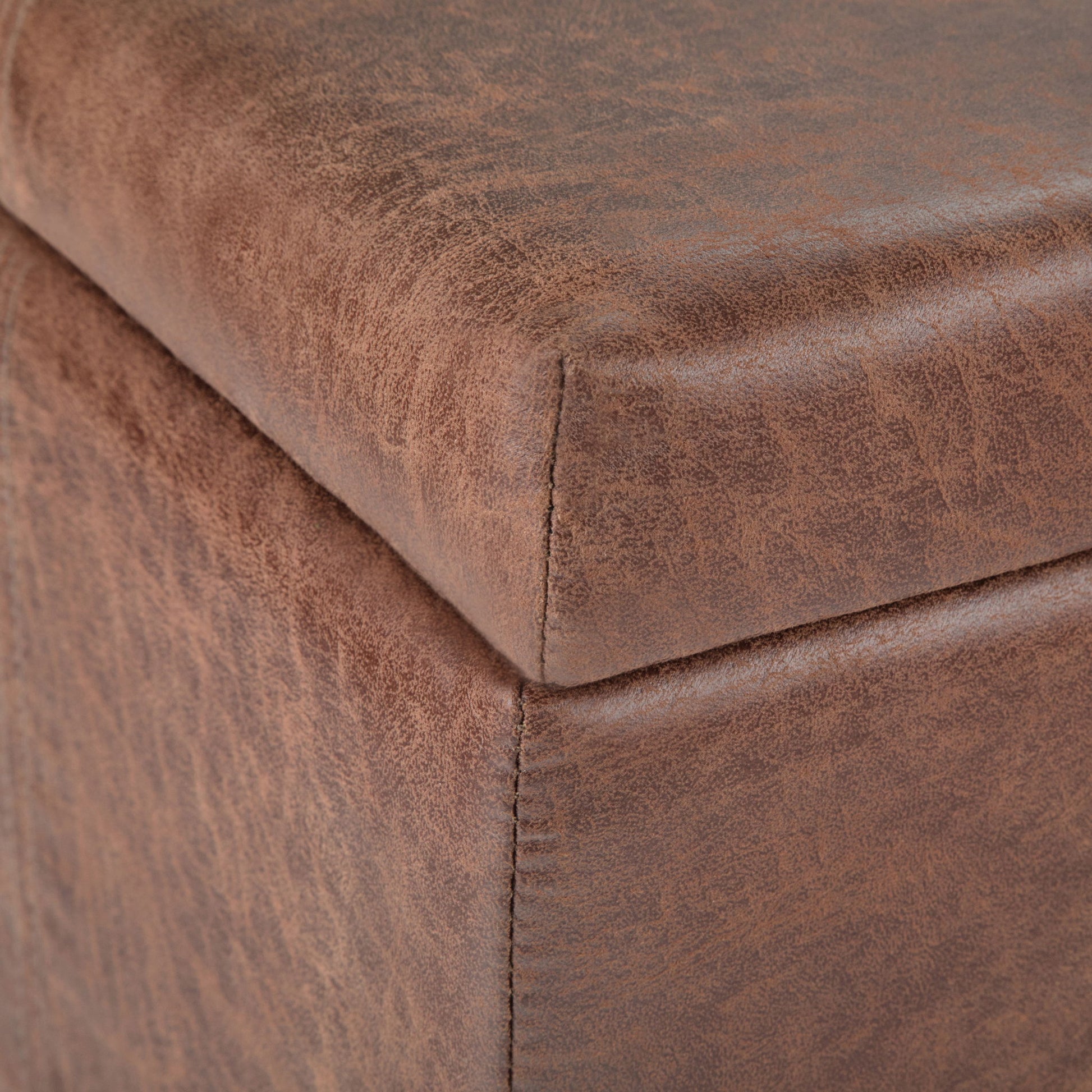 Close-up of the corner of the Dover - Upholstered Storage Ottoman Bench, highlighting its brown faux leather texture and precise stitching along the edge.