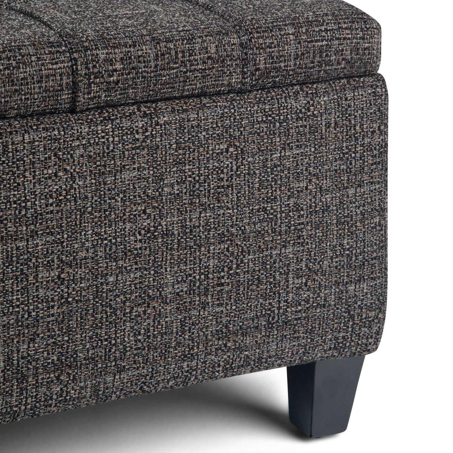 Close-up of the Harrison - Upholstered Coffee Table Storage Ottoman corner, showing textured dark gray and brown fabric upholstery with short, angled black wooden legs.