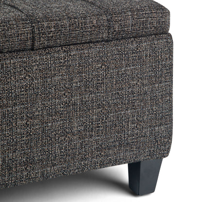 Close-up of the Harrison - Upholstered Coffee Table Storage Ottoman corner, showing textured dark gray and brown fabric upholstery with short, angled black wooden legs.