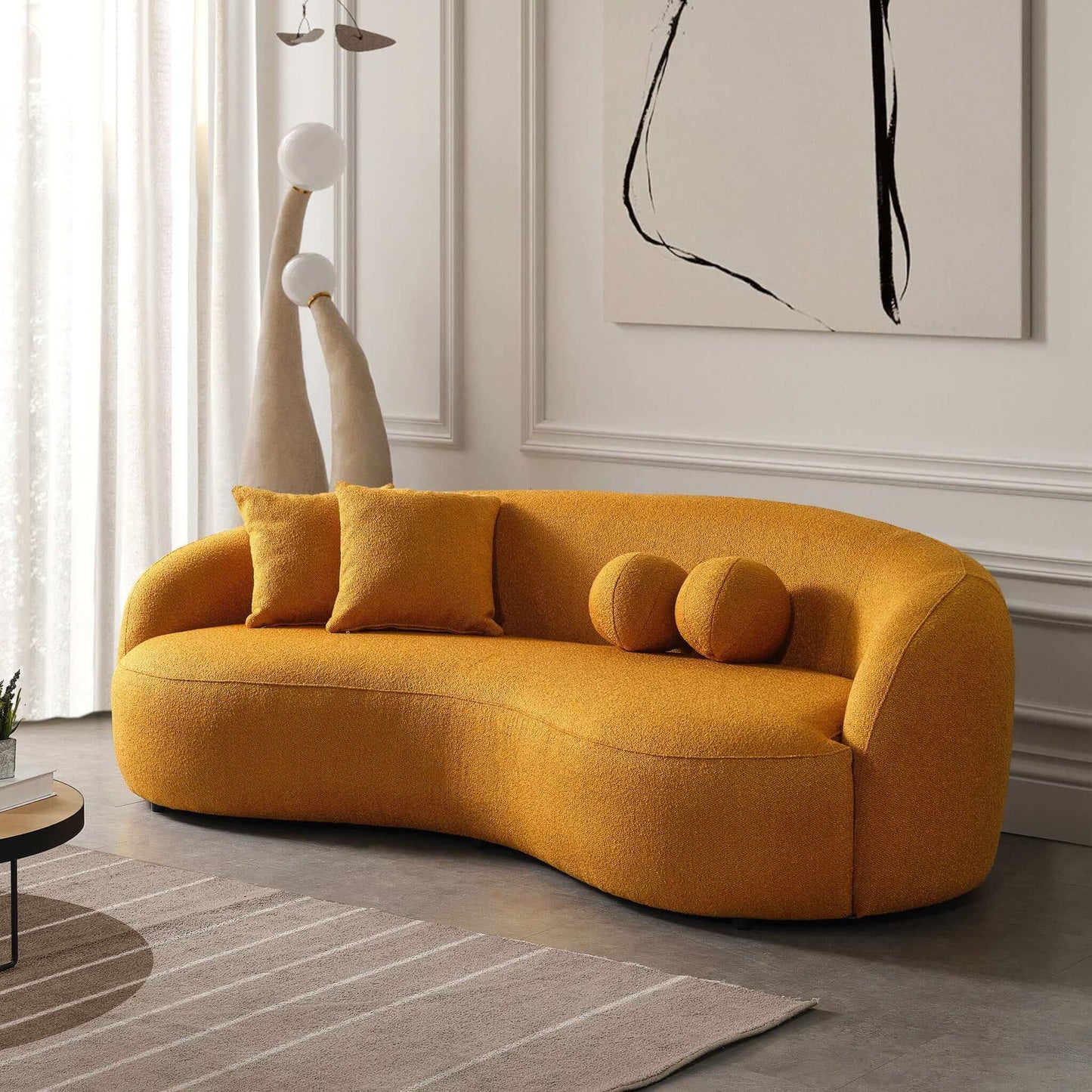 A modern living room featuring the Drake - Japandi Style Curvy Boucle Sofa in mustard-yellow, paired with matching pillows, abstract wall art, sculptural floor lamps, and a rug on a gray floor.