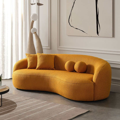 A modern living room featuring the Drake - Japandi Style Curvy Boucle Sofa in mustard-yellow, paired with matching pillows, abstract wall art, sculptural floor lamps, and a rug on a gray floor.