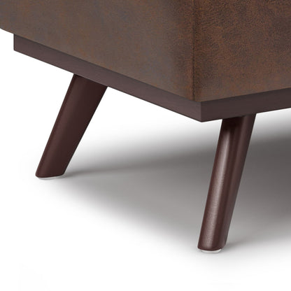 Close-up of two dark brown angled wooden legs supporting the Owen Lift Top Large Coffee Table Storage Ottoman, featuring brown textured fabric upholstery and casting a soft shadow on a white surface.