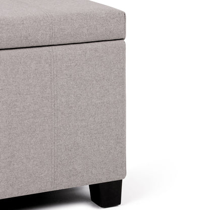 Close-up of the corner of the Dover - Upholstered Storage Ottoman Bench in light gray fabric with black wooden legs, shown against a white background.