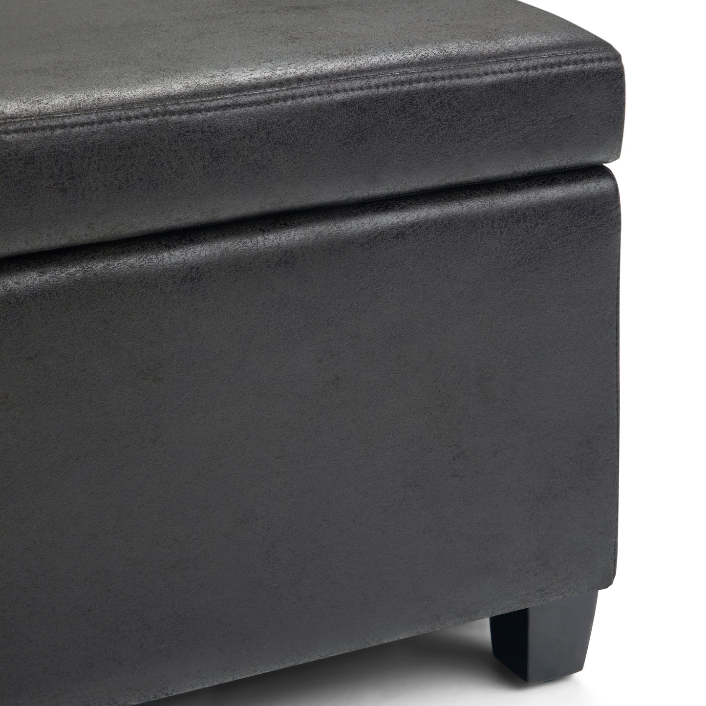 Close-up of the corner of the Avalon - Storage Ottoman Bench in distressed black faux leather, featuring visible stitching and short black legs that highlight its texture and material.