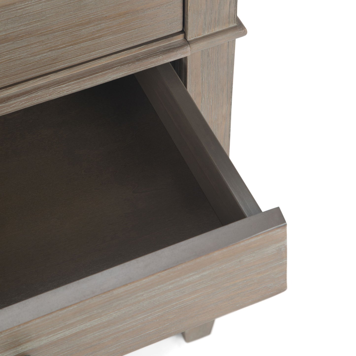 A close-up of the Carlton - Bedside Table, Handcrafted, shows a partially open wooden drawer with a light brown, weathered finish and reveals the inside along with part of the furniture’s frame.