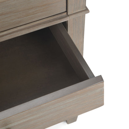 A close-up of the Carlton - Bedside Table, Handcrafted, shows a partially open wooden drawer with a light brown, weathered finish and reveals the inside along with part of the furniture’s frame.