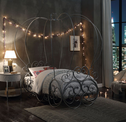 A whimsical bedroom features the Priya Twin Bed With Canopy in silver, boasting delicate metal scrollwork, soft bedding, string lights on gray walls, and a large window revealing a nighttime cityscape.