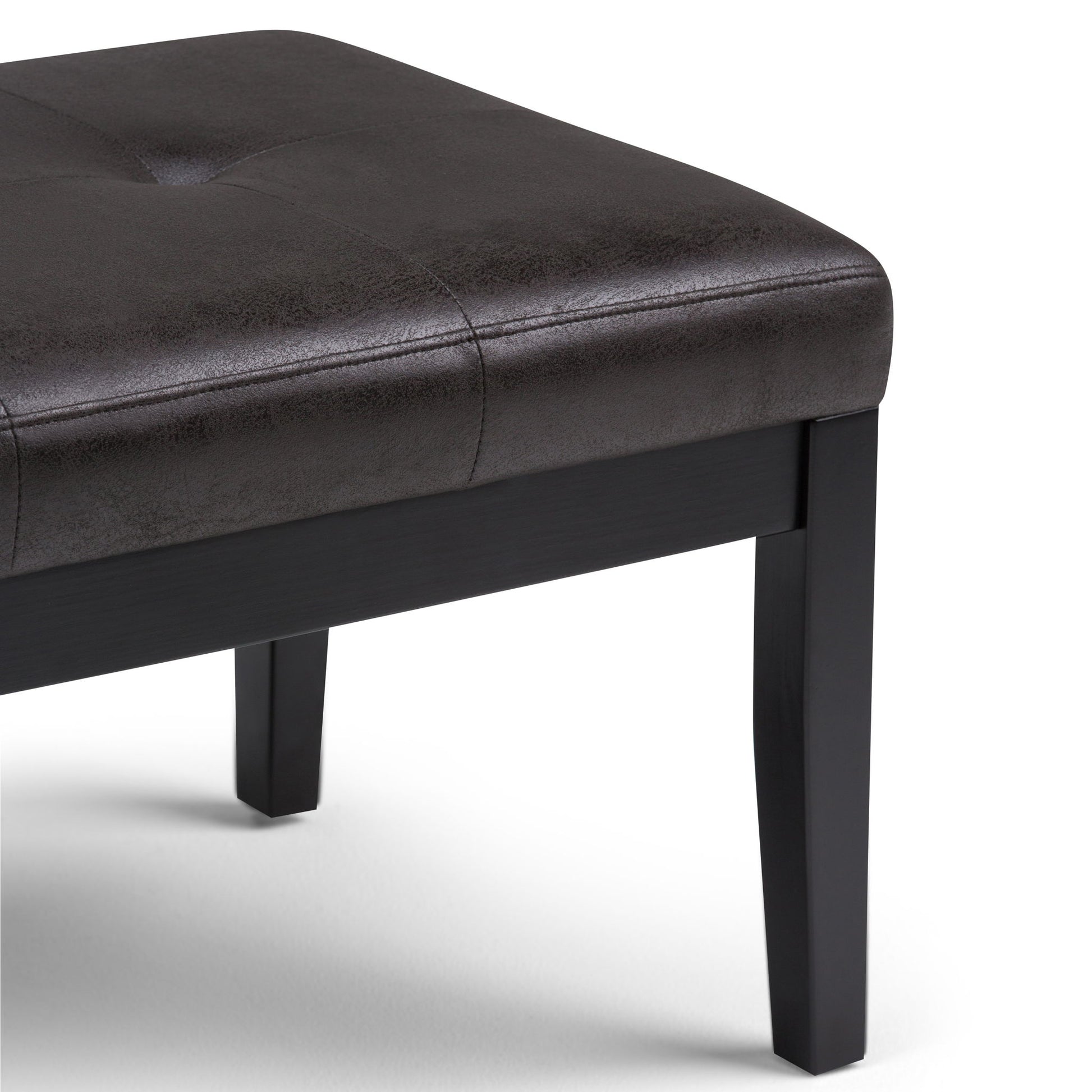 The Lacey Upholstered Tufted Ottoman Bench features a dark brown faux leather seat and black wooden legs, shown close-up against a white background.