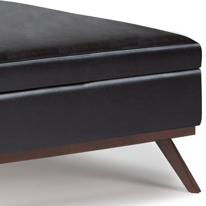 Close-up of the corner of the Owen - Multifunctional Square Coffee Table Storage Ottoman in black upholstery, featuring a dark wooden angled leg, shown against a white background.