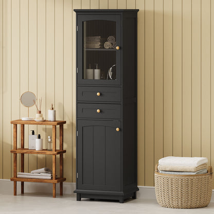 A tall bathroom storage cabinet with glass doors, two drawers, and adjustable shelves stands against a beige paneled wall. Nearby are a small wooden shelf with toiletries and a basket of folded towels on the floor.