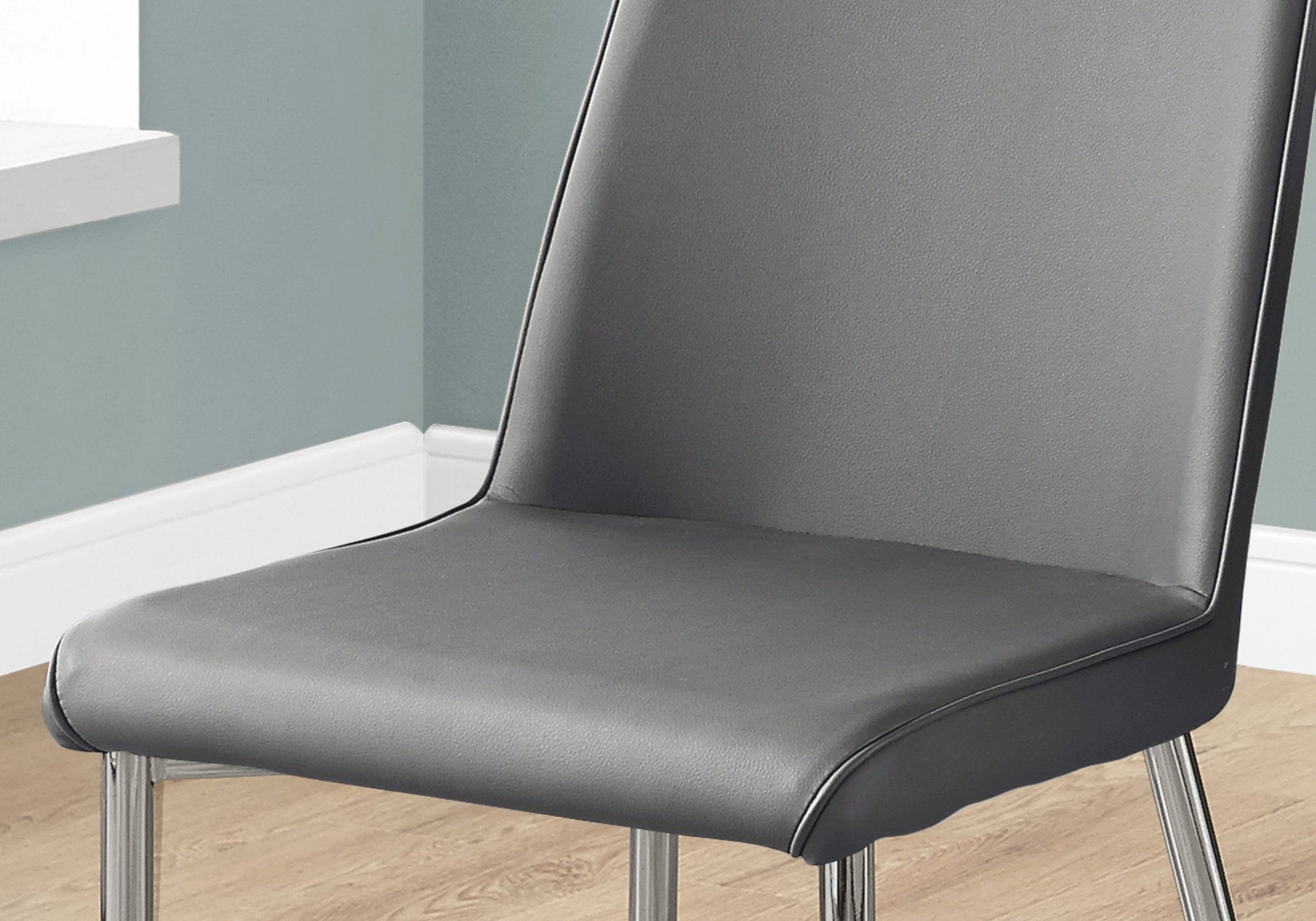 A close-up of the Contemporary Upholstered Dining Side Chair (Set of 2), featuring a padded seat and backrest with metal legs, shown on a wooden floor beside a light blue wall and white baseboard.
