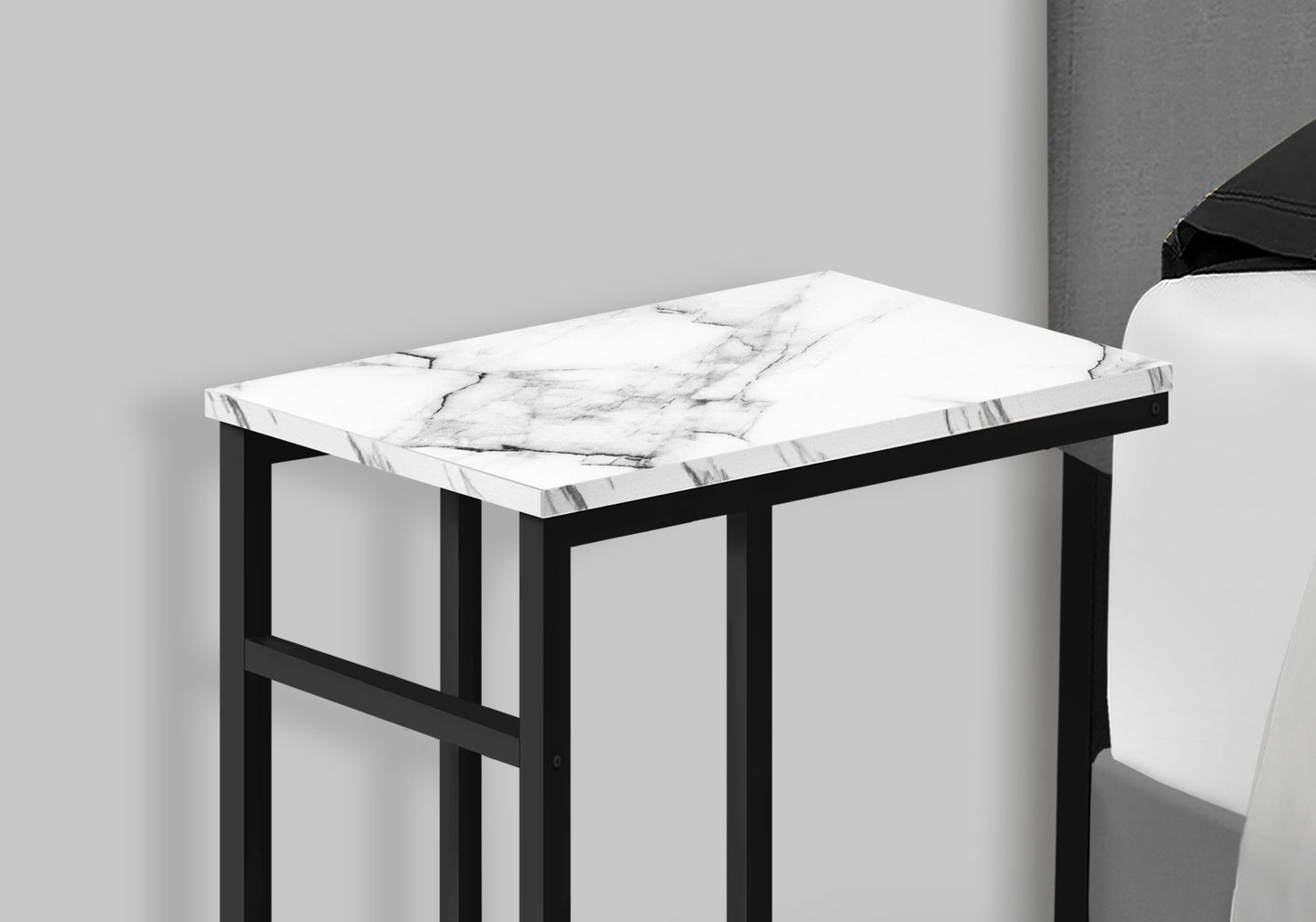 The Accent Table, C-shaped with a white marble top and black metal frame, sits beside a light-colored sofa against a gray wall for a contemporary and modern look.
