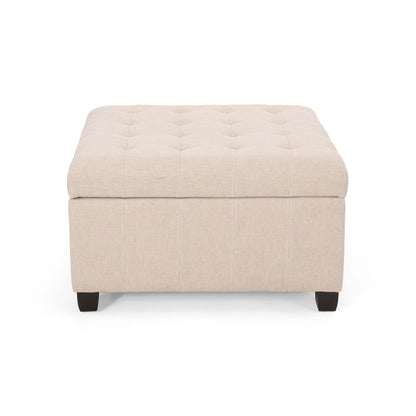 The Isabella Contemporary Ottoman With Storage is beige, square, and tufted, featuring short dark wooden legs and shown from the front against a white background.