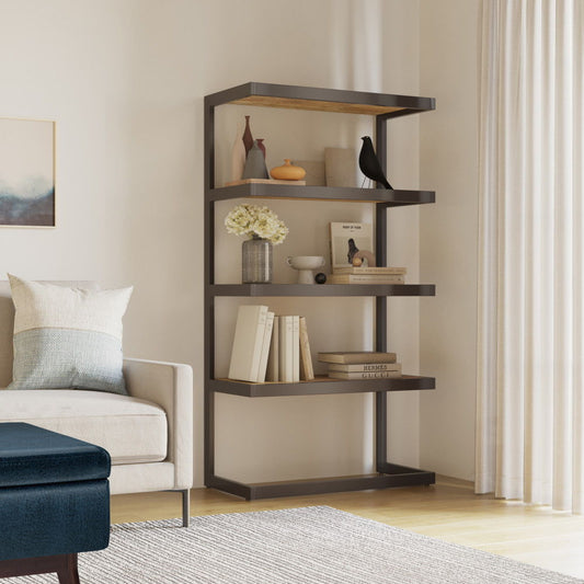 The Erina - Handcrafted Bookcase with dark wooden shelves displays books, a vase, framed photos, and decor. It stands beside a light sofa and sheer curtains in a bright living room.
