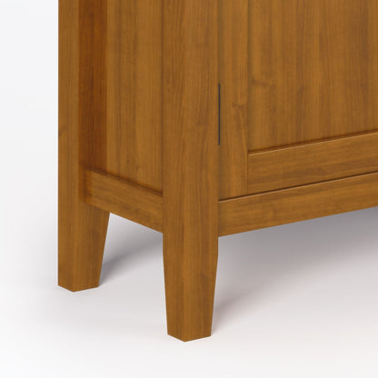Close-up of the lower corner of the Redmond - Handcrafted Low Storage Cabinet, featuring a honey-brown finish, two square legs, and part of the cabinet door set against a plain white background.