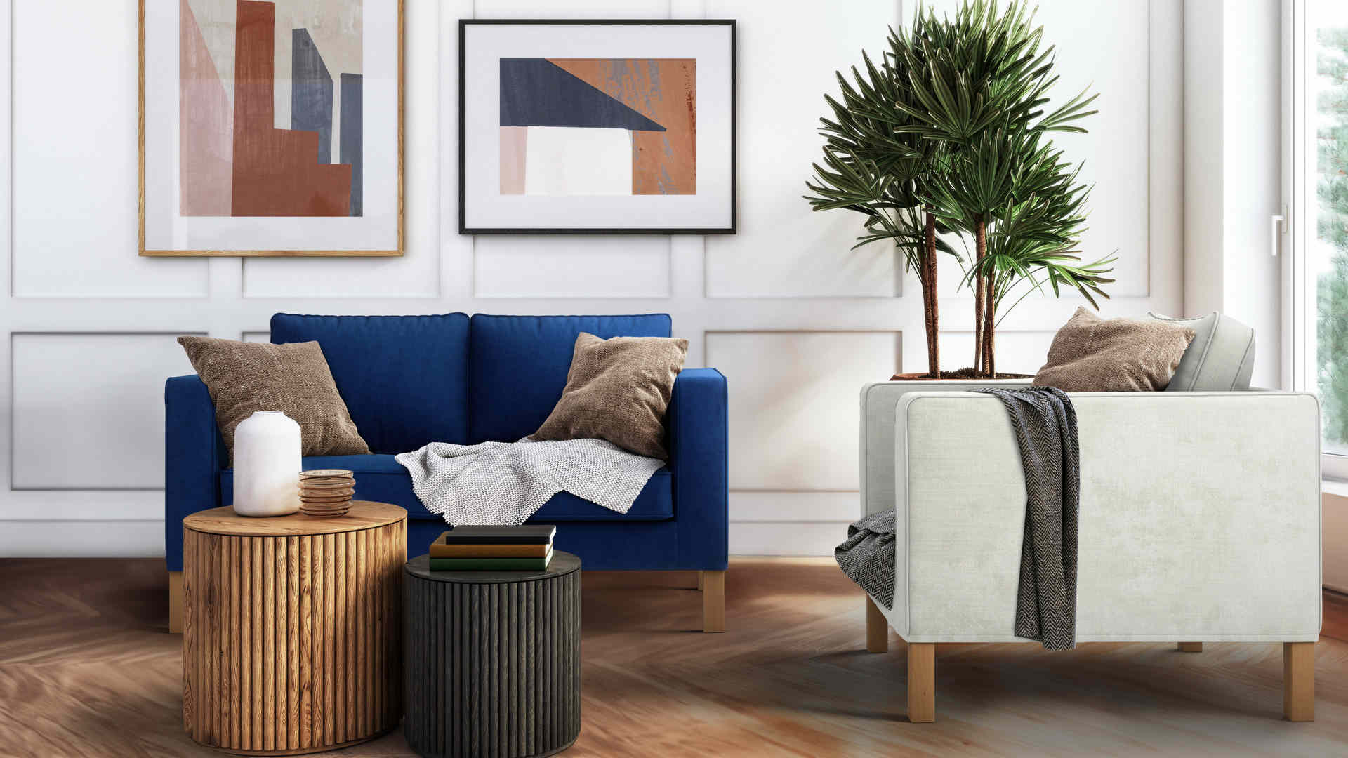 A modern living room featuring a blue sofa with brown and gray pillows, a white armchair, a large potted plant, round wooden coffee tables with a candle and books, and abstract art on the wall. Light streams in through a large window, illuminating the space.