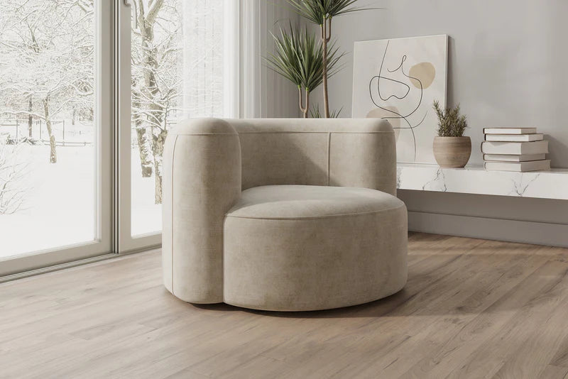 A modern living room featuring the Mellow Sectional Sofa by Acanva in a light beige, set elegantly on a wooden floor. Large windows frame a snowy landscape outside, while a minimalist plant sits on a shelf adorned with stacked books and abstract art hangs on the wall.
