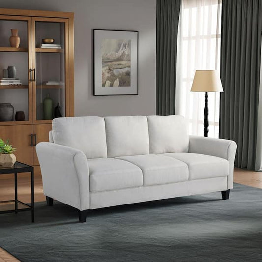 A Lifestyle Solutions Wesley 80.3 in. dark grey 3-seater sofa sits on a blue-green rug in a living room with a wooden cabinet, framed art, floor lamp, and green curtains by large windows.