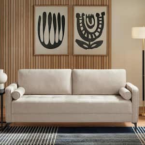 A modern living room showcases the StyleWell Goodwin Mid-Century Modern Sofa, complete with throw pillows and cylindrical armrests. Two abstract black-and-white artworks are mounted on the wooden paneled wall behind it. To the right, a floor lamp provides illumination, and a portion of a rug is visible on the floor.