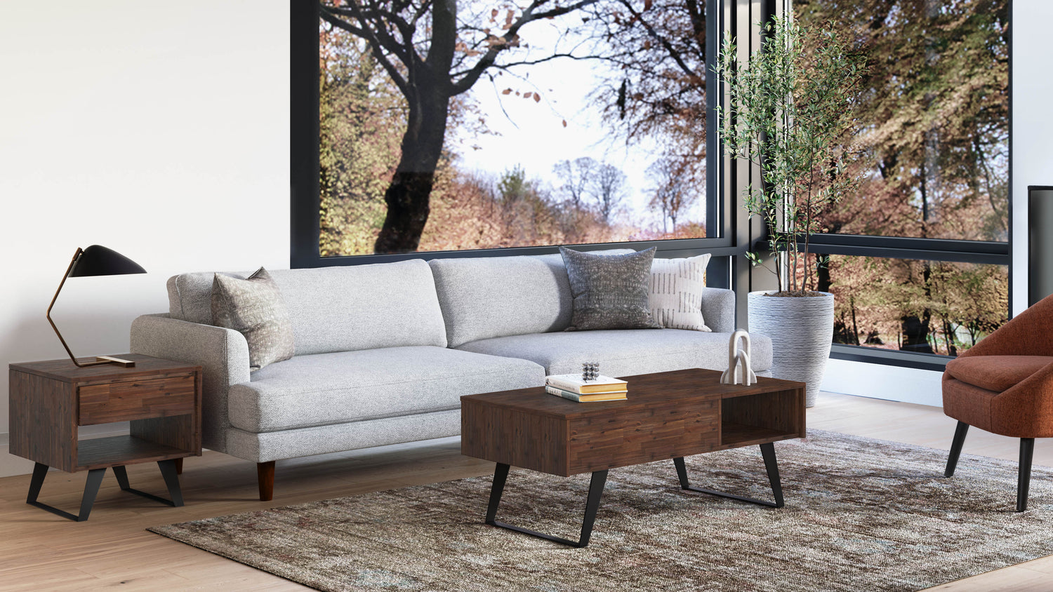 A modern living room with a large window showcasing a view of trees. The room has a light gray sofa with decorative pillows, a wooden coffee table and side table with black legs, a potted plant, a unique table lamp, and an armchair upholstered in burnt orange fabric.