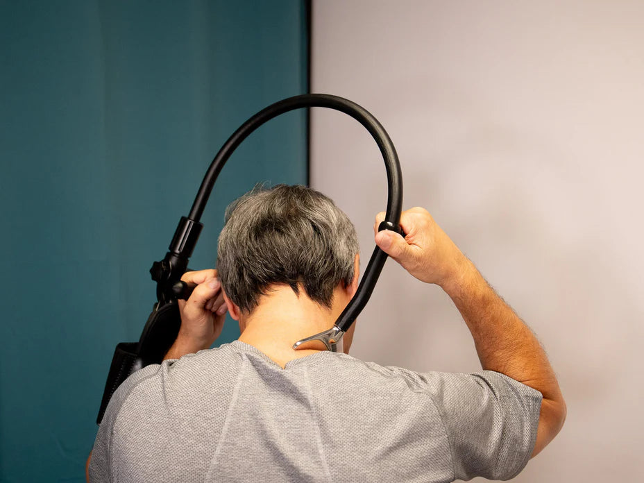 A person with short gray hair is seen from behind, holding a stethoscope over their neck. They are wearing a gray shirt, and the background is split into two colors: teal on the left and light gray on the right.